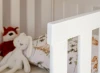 Biała barierka ochronna łóżka dziecięcego z widocznymi w tle pluszowymi zabawkami.