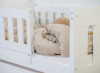 Białe drewniane łóżko dziecięce z barierką i przytulną beżową pościelą.