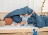 Dziecko bawiące się pod niebieską kołdrą na niskim łóżku parterowym.