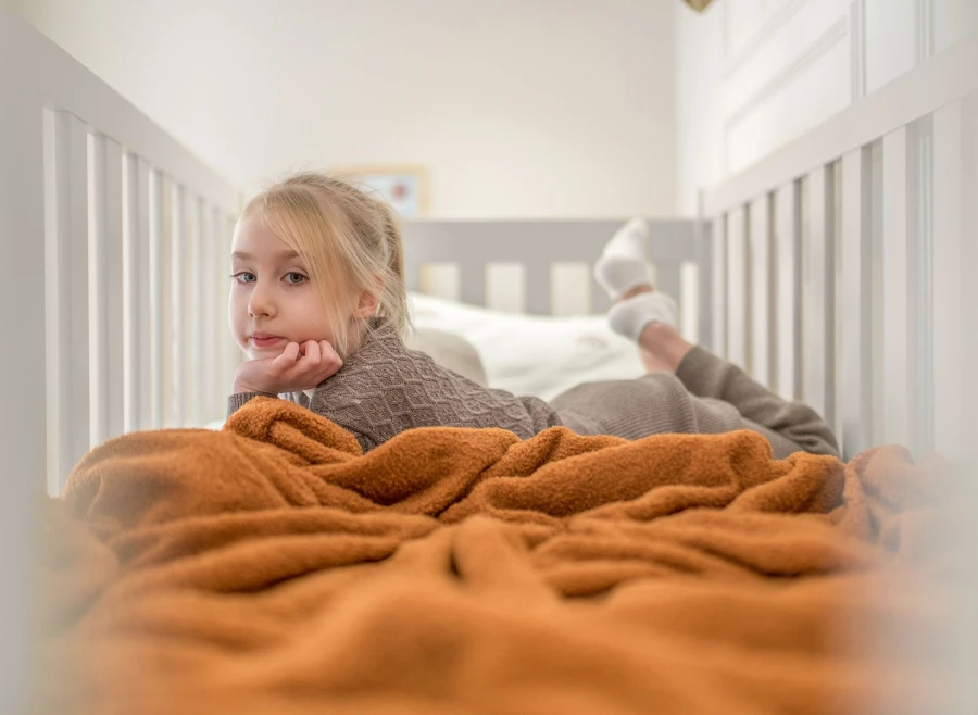 Komfortowe łóżko antresola dla dzieci z miękkimi poduszkami i pomarańczowym kocem.